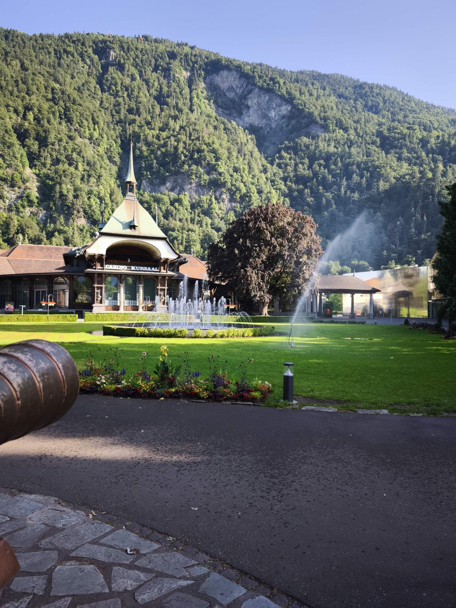 Casino Kursaal and Höhematte park with fountain in Interlaken beneath forested alpine cliffs