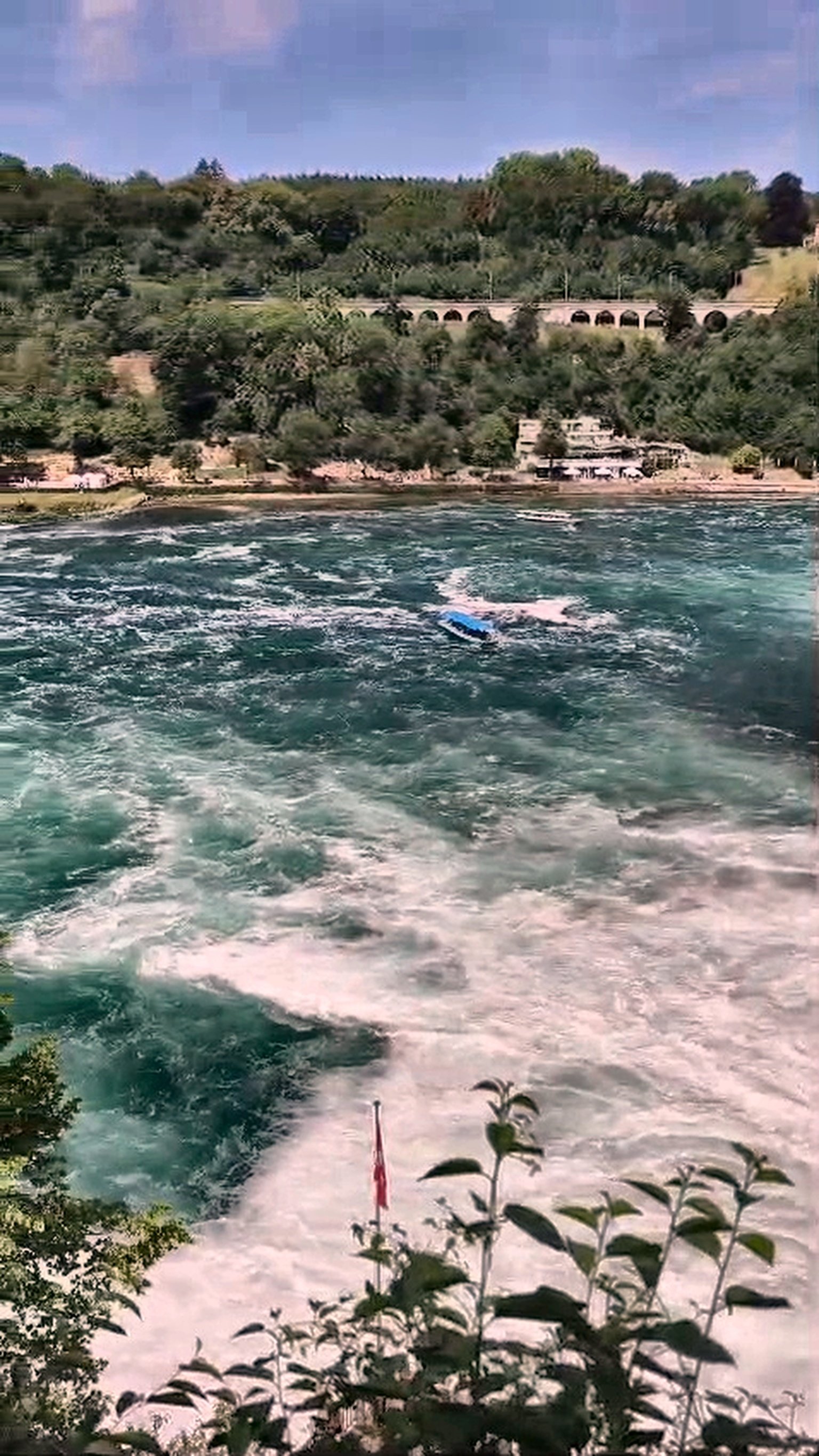 Rhine Falls rapids with stone railway bridge and tour boat on the turquoise Rhine River